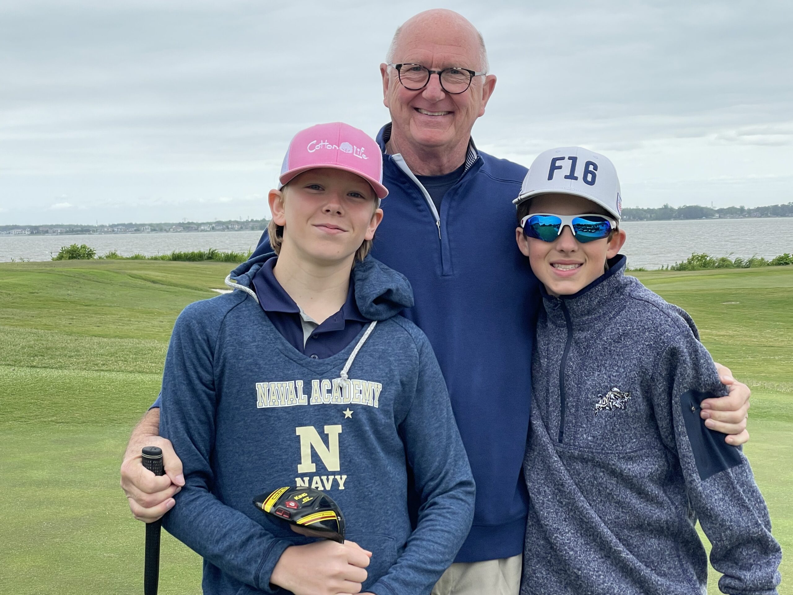 Three golfers posing on the course by the water