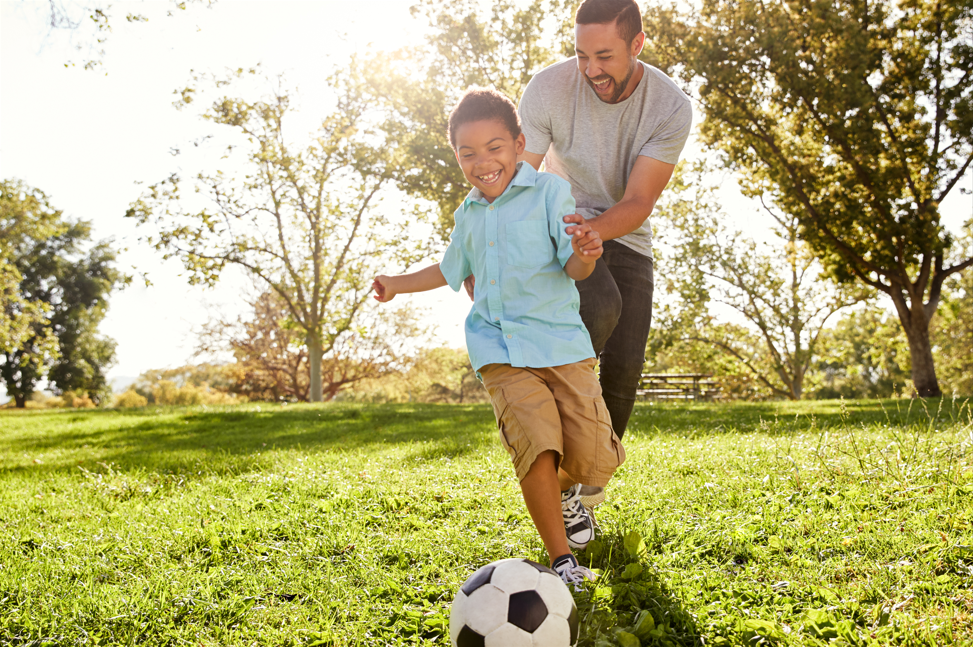 Father and son playing soccer in a park